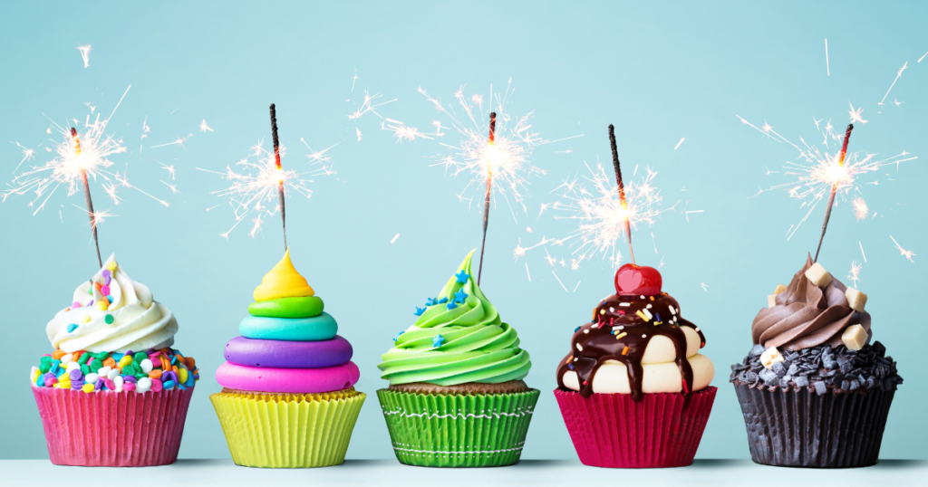 Five different coloured cupcakes with sparklers in each depicting a celebration